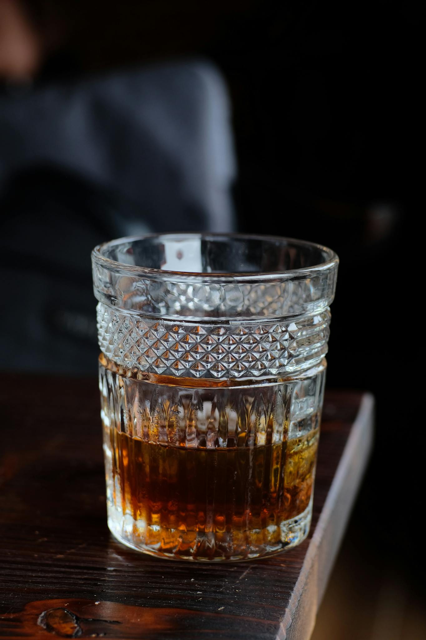 Close-up of whiskey in a crystal glass on a dark wooden table with a blurred background.